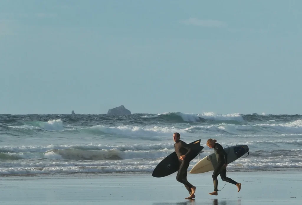 Surfers running along the beach at Watergate Bay