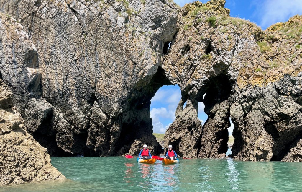 Kayakers paddling under natural limestone arch.