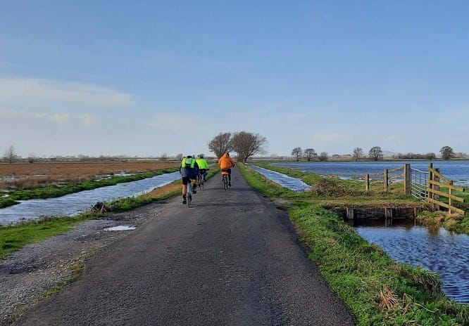 Cyclists on flat trail at Steart marshland.