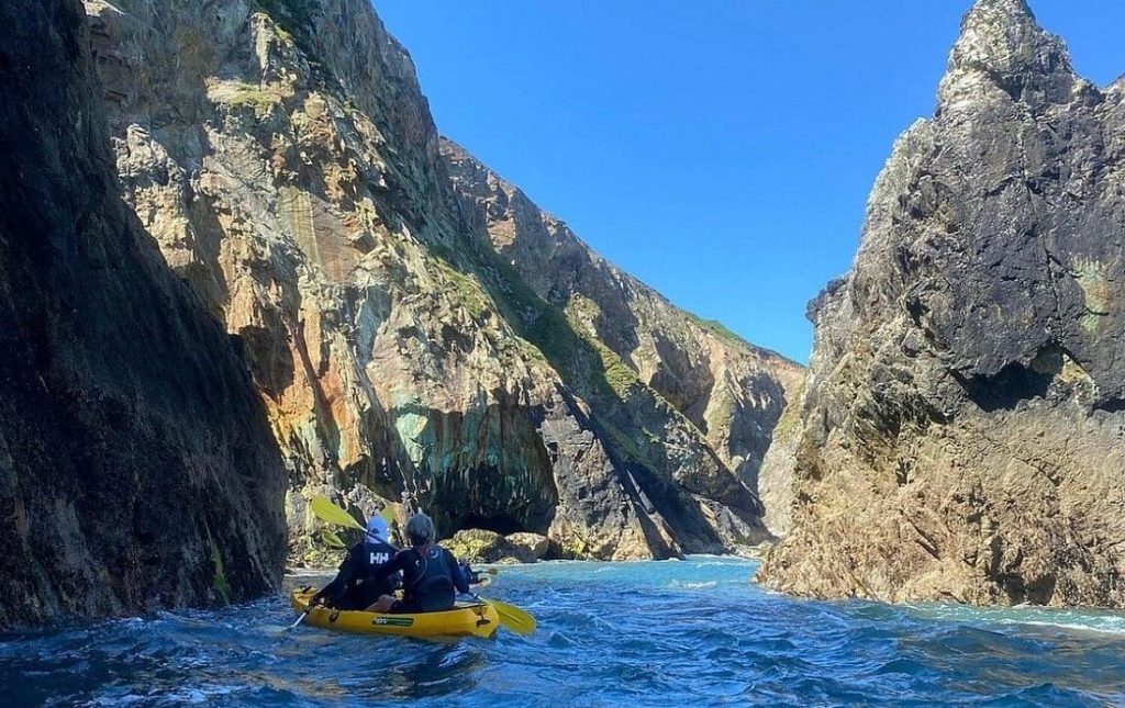 Kayaker paddling beside coastal cliffs.