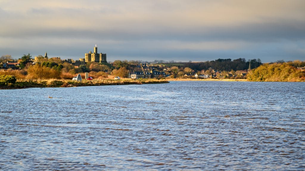 Warkworth Castle rising above the River Coquet surrounded by greenery
