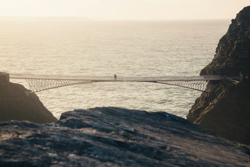 Couple walking across Tintagel's cantilever bridge as the sun sets