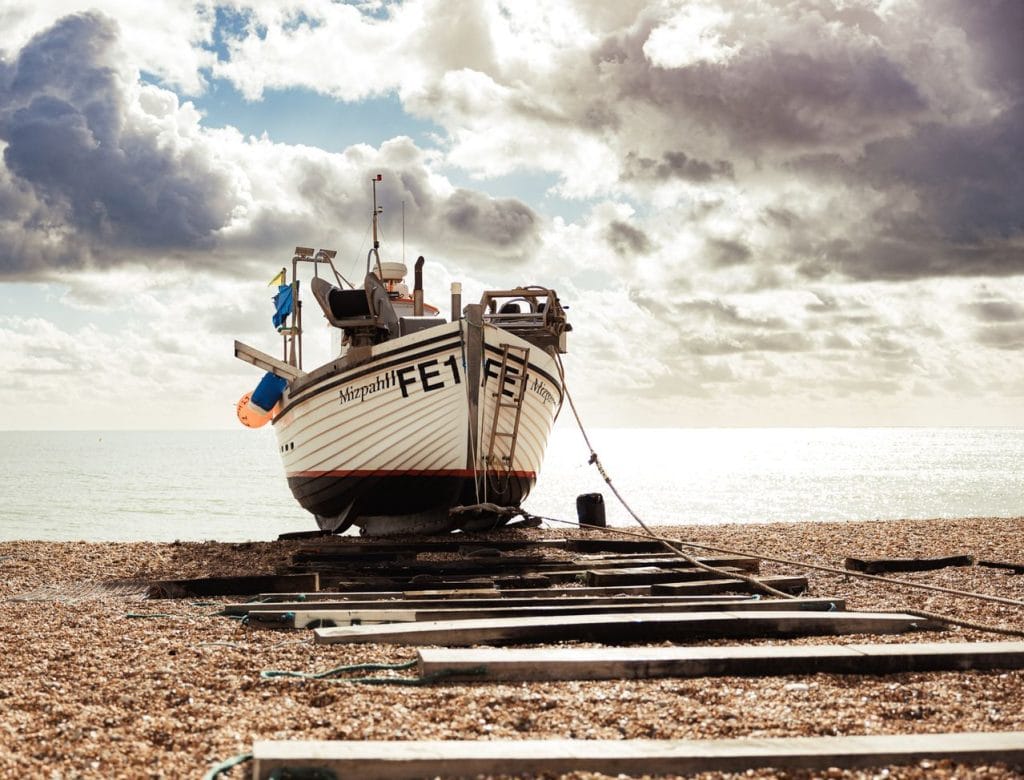 Fishing boat on Hythe beach with a cloudy sky and pebble shore.