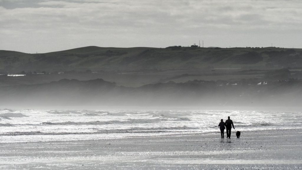 Couple walking their dog along Filey beach in Yorkshire.
