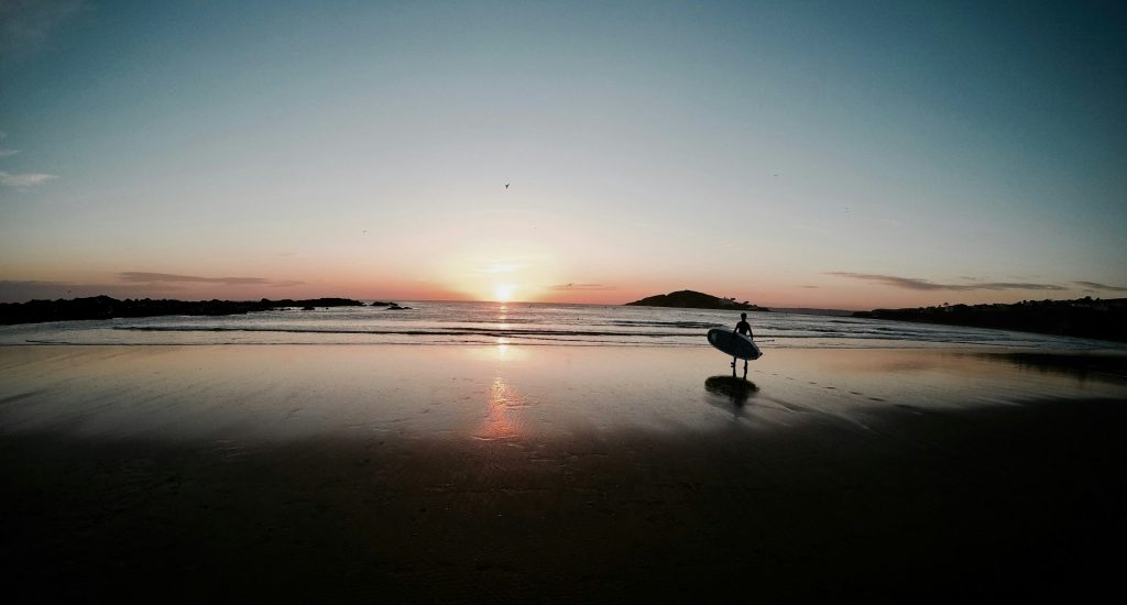 A paddleboarder walking on Bantham Beach in South Devon at sunrise.