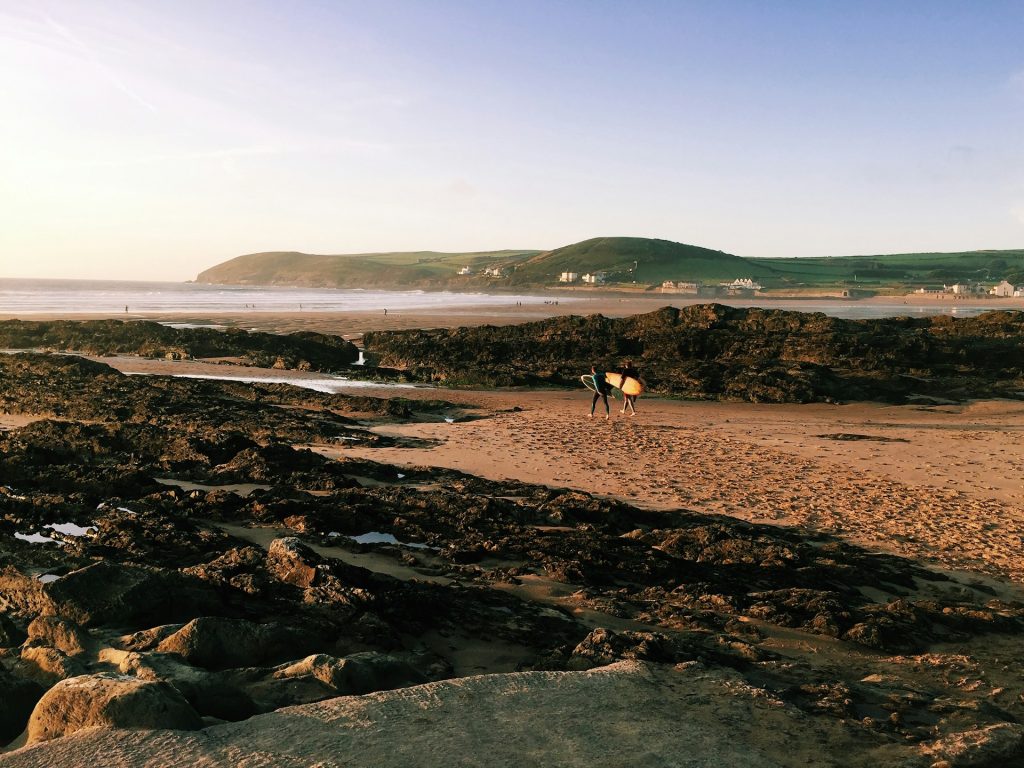 Two surfers with boards walking on Croyde Bay Beach, North Devon.