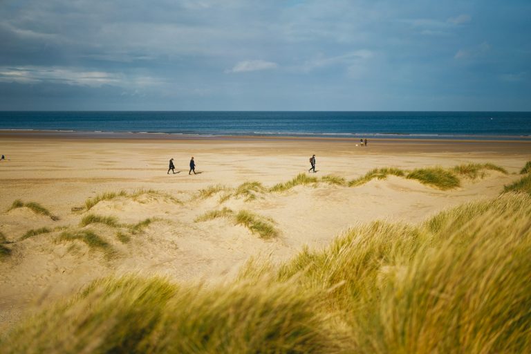 View of Holkham Beach from the grassy dunes with people walking on the sand.