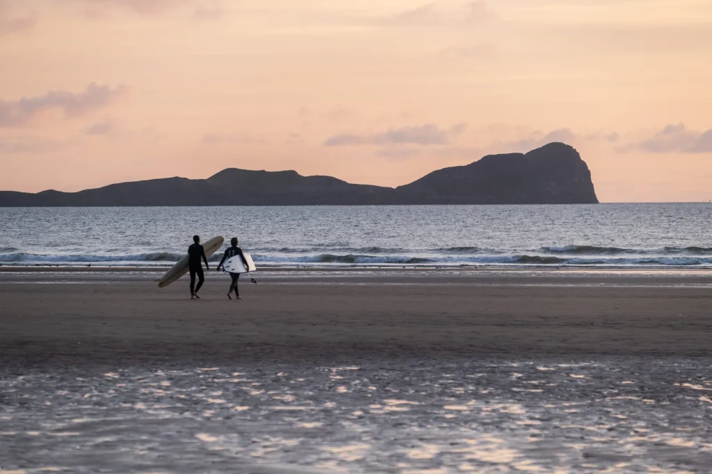 Two surfers with boards looking at the waves at Llangennith, Gower.