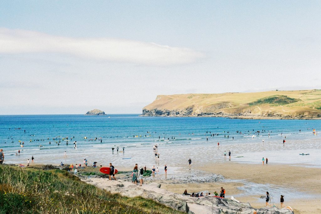 Summer scene at Polzeath Beach with surfers and families.