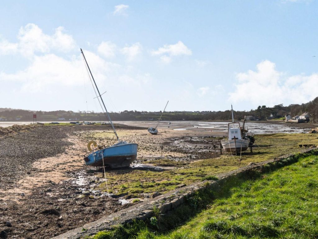 Three boats sitting high and dry on Red Wharf Bay during low tide.