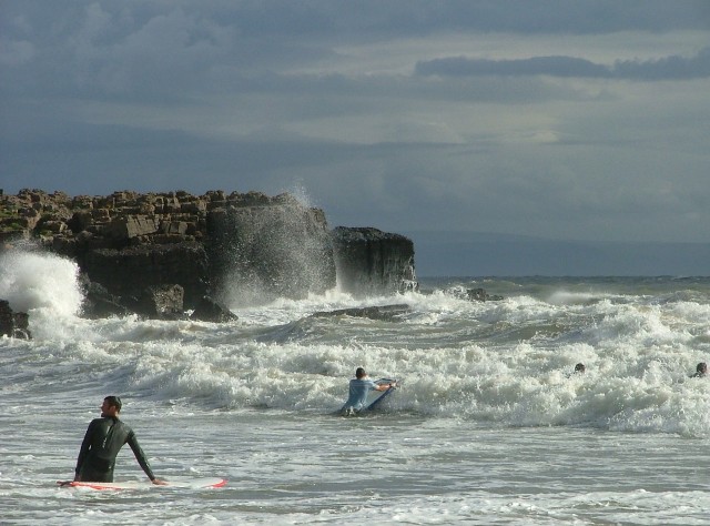 Surfer and bodyboarder heading out into the waves on Rest Bay, Porthcawl, Wales.