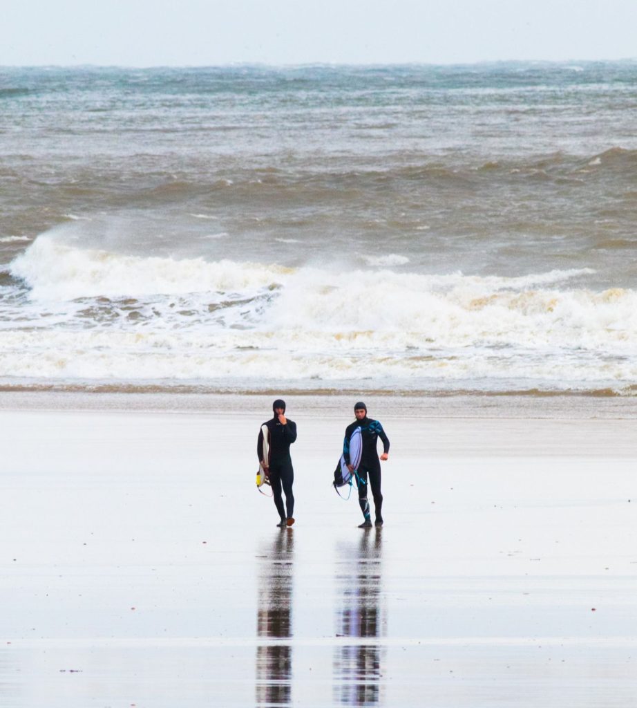 Two surfers coming out of the sea in Saunton Sands, Devon, UK.