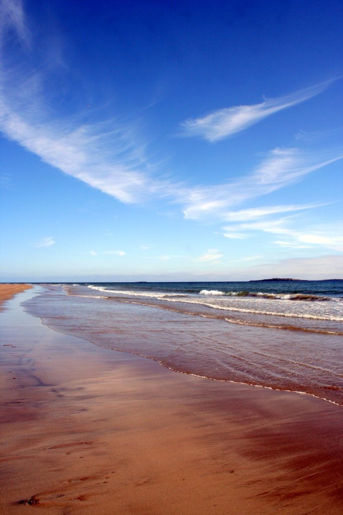 An empty Seahouses beach in autumn under a blue sky.