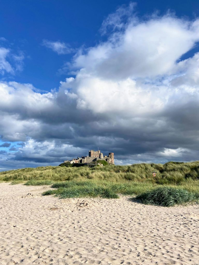View from the beach of Bamburgh Castle under menacing grey clouds.