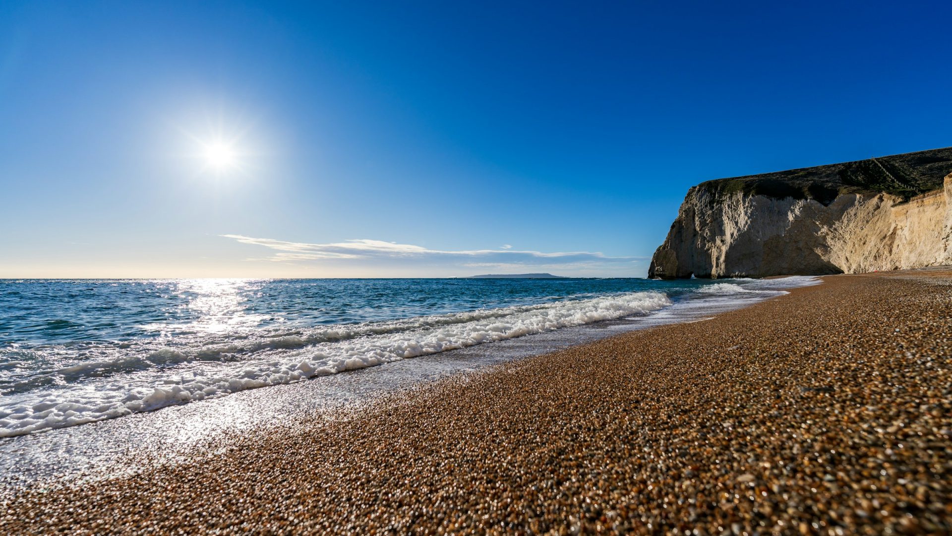 Shingle beach glistening in the winter sun, below a pale cliff on the Jurassic Coast, Dorset.