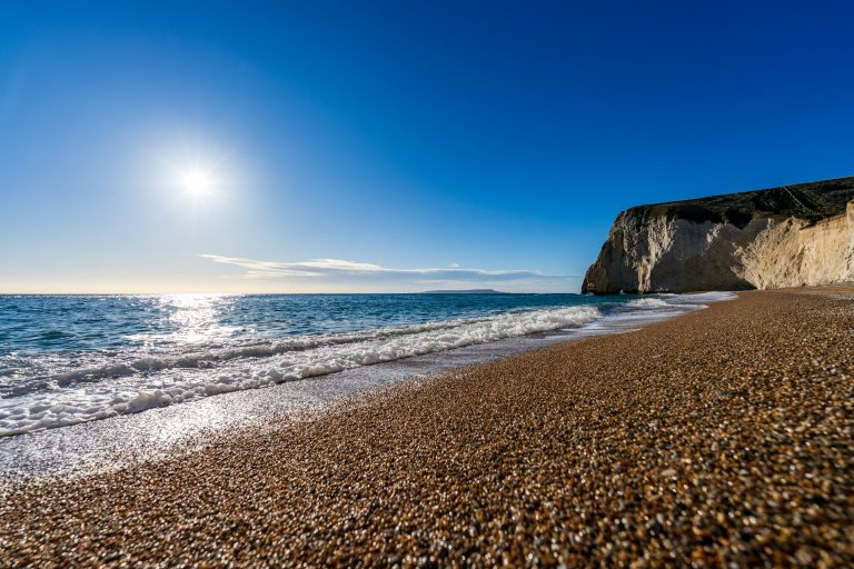 Shingle beach glistening in the winter sun, below a pale cliff on the Jurassic Coast, Dorset.