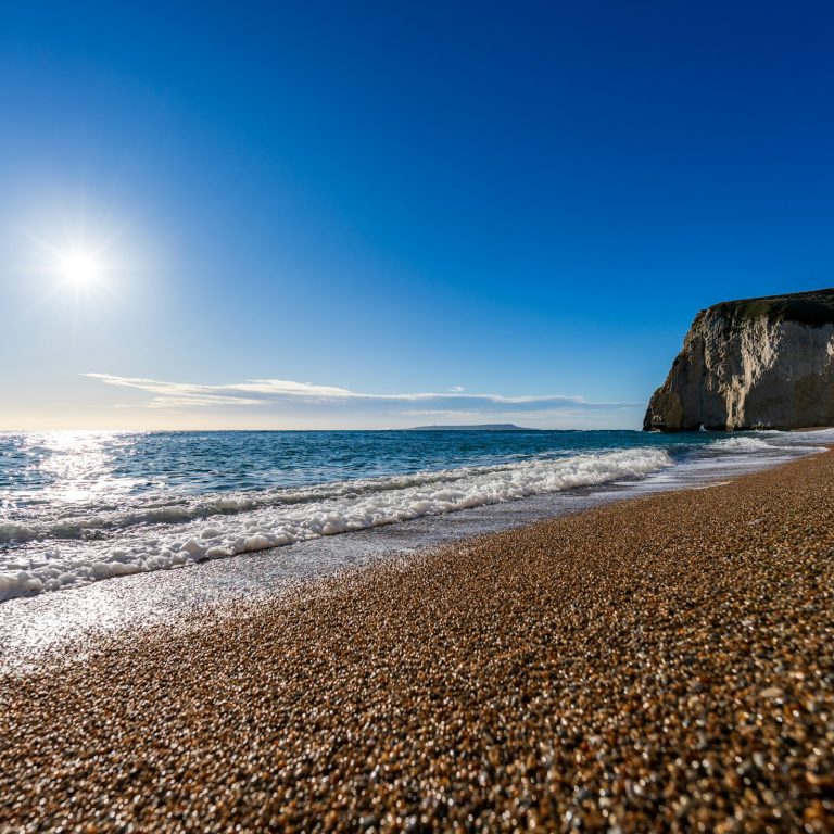 Shingle beach glistening in the winter sun, below a pale cliff on the Jurassic Coast, Dorset.